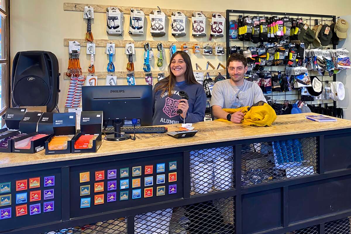 Dos empleados sonrientes en el mostrador, con equipo de escalada y gorras colgadas detrás
