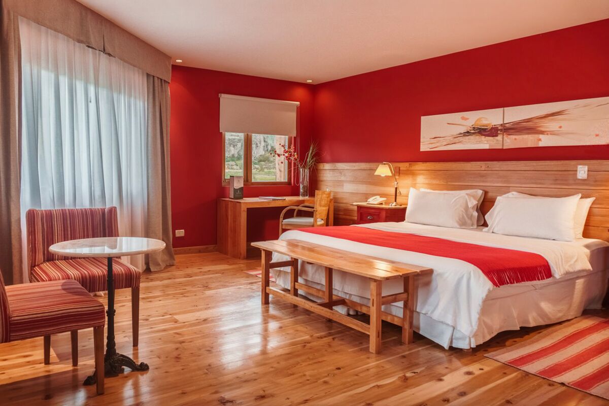 Room with red walls, a double bed with a red throw, a table with two armchairs and wooden floors