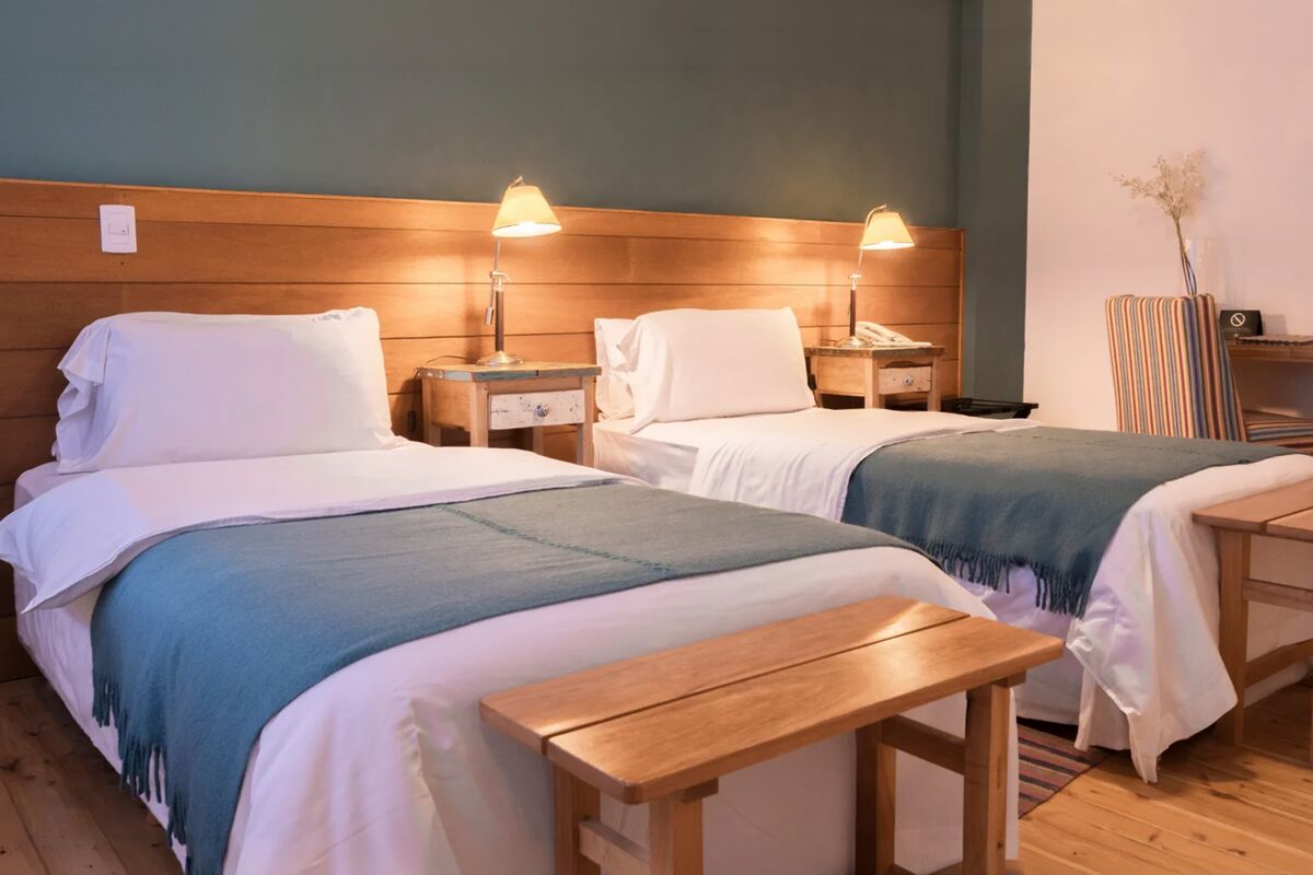 Room with two single beds with blue throws and a wooden bench at the foot