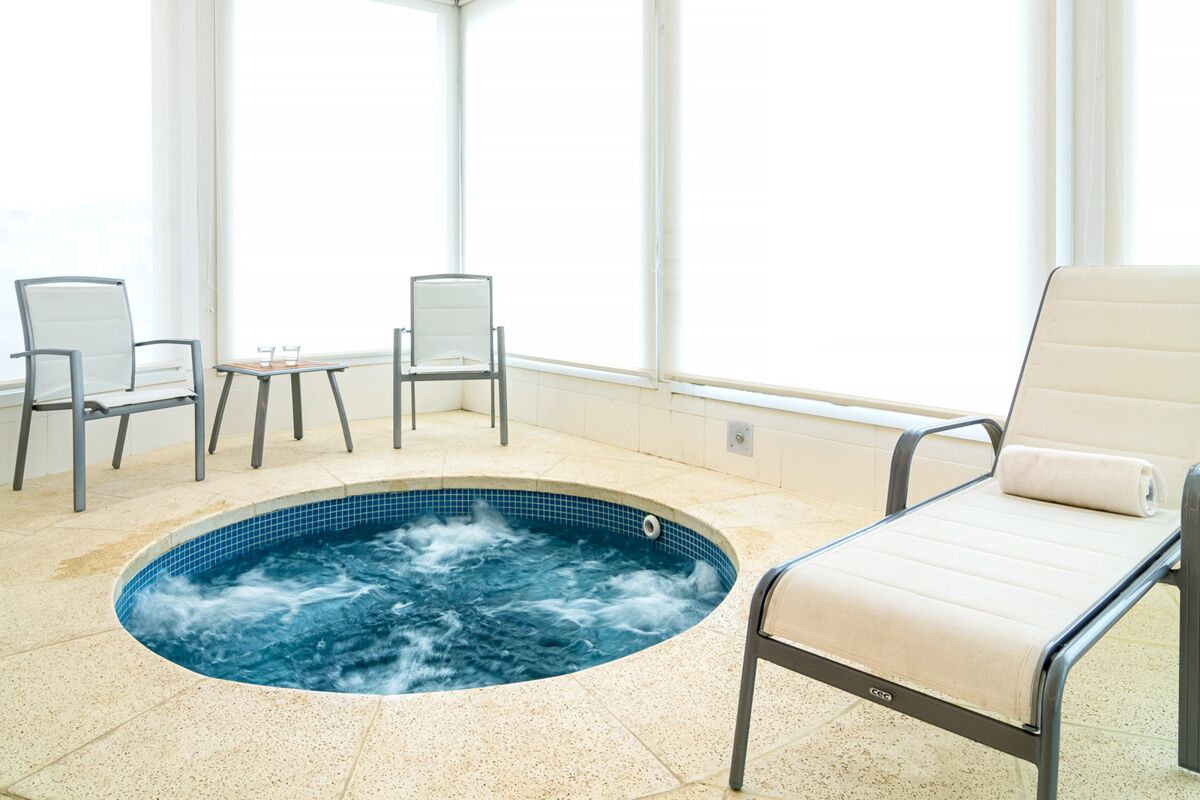 Round jacuzzi next to a lounger and chairs in front of large windows