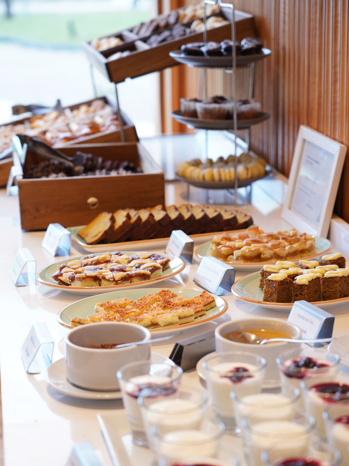 Buffet table with loaf cakes, tarts, pastries and small cups of yogurt