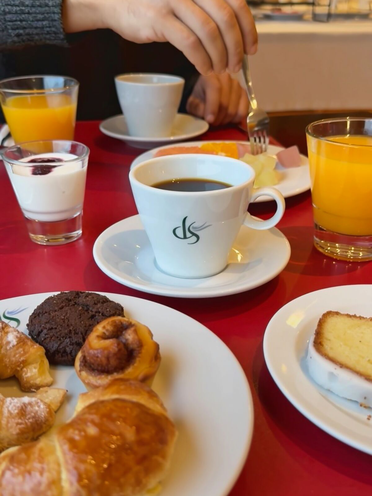 Breakfast table with a coffee cup bearing the hotel logo, orange juice, yogurt and croissants
