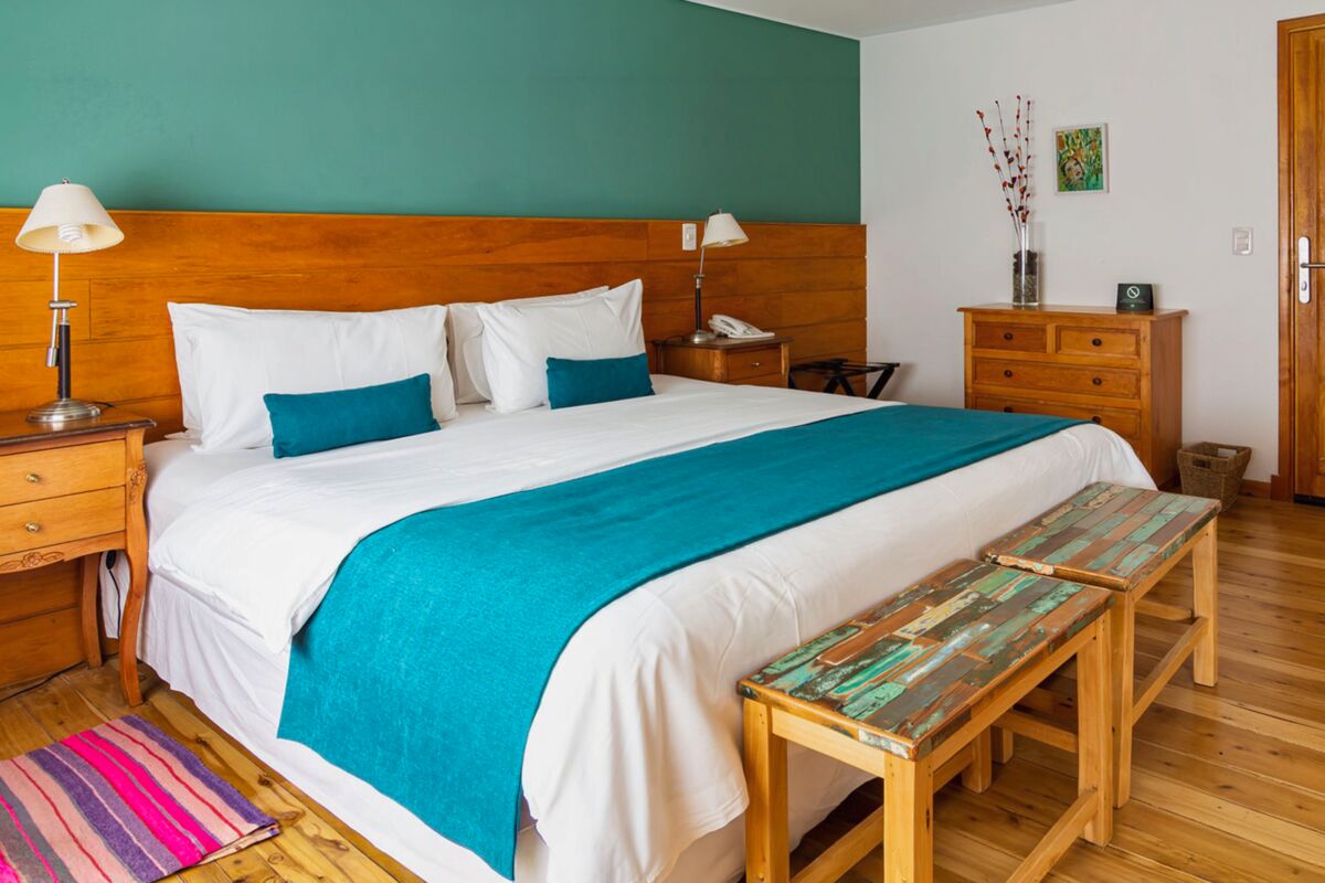 Room with a green wall, a double bed with a turquoise throw and two wooden benches