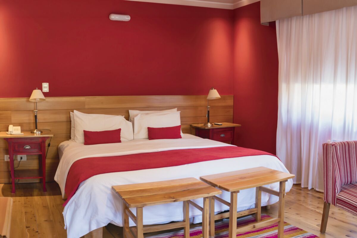 Room with red walls, a double bed with red cushions and white curtains