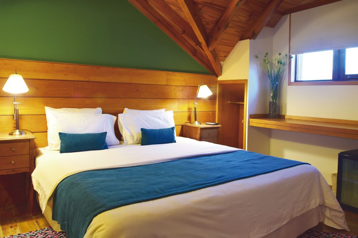 Room under a pitched wooden ceiling, with a green wall, a double bed and a window