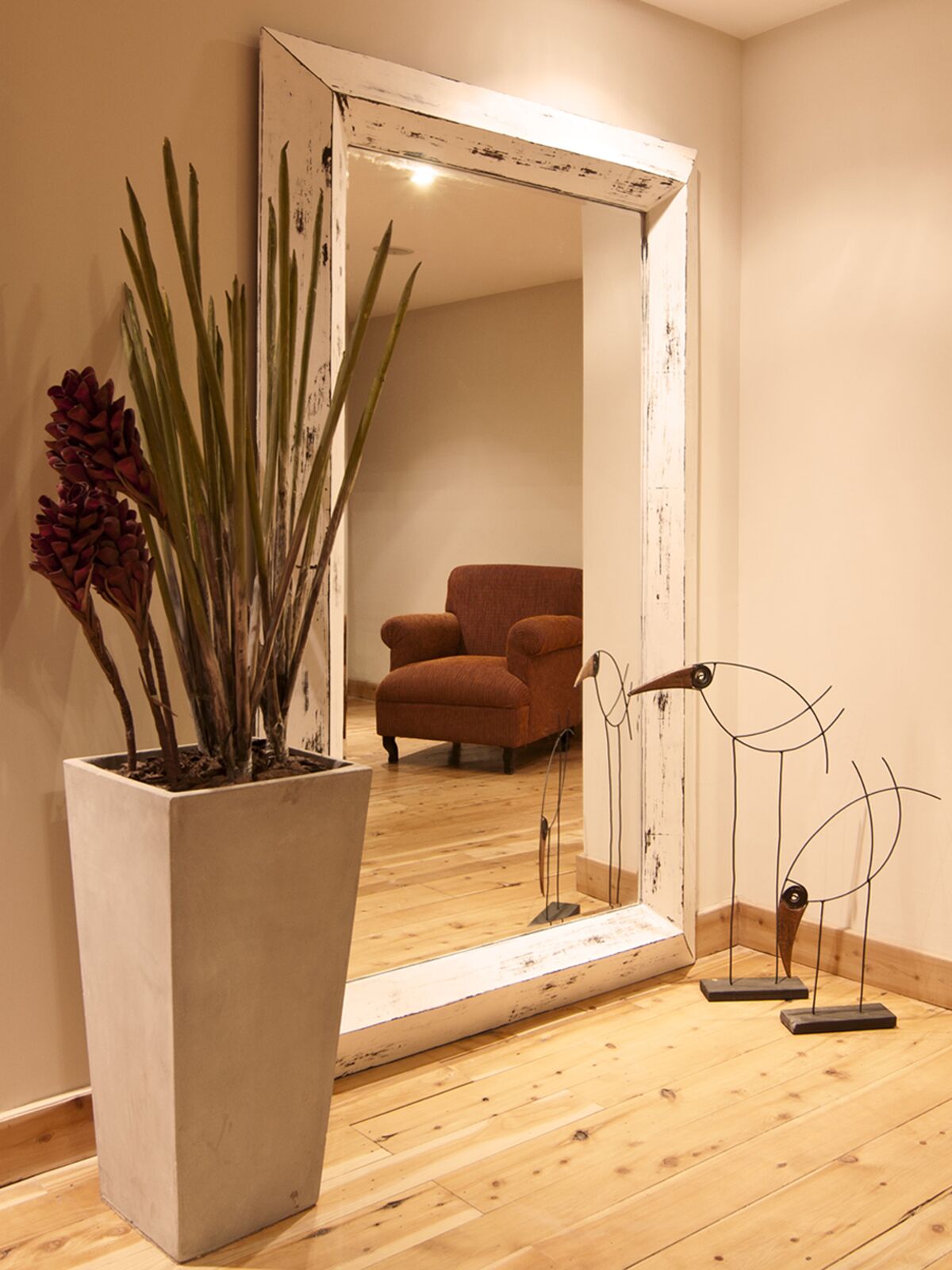 Mirror with a white wooden frame, a potted plant and an armchair in the background