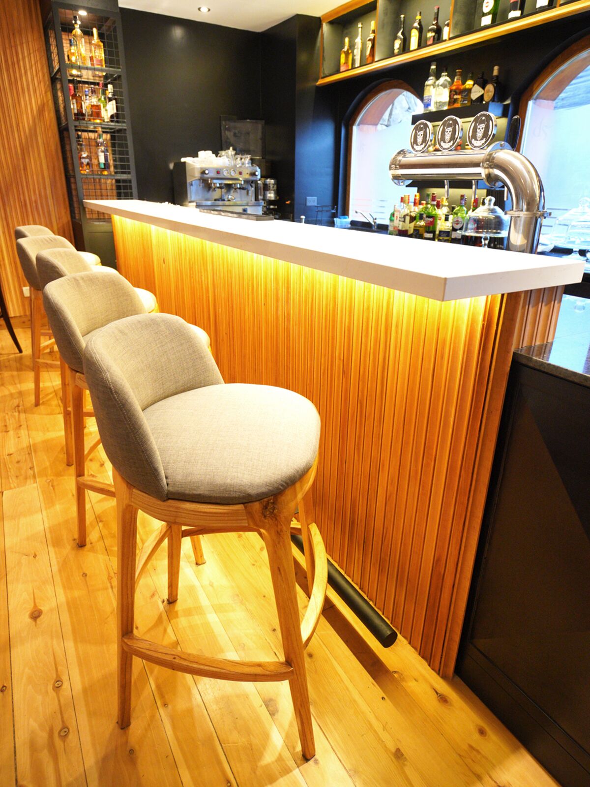 Lit bar counter with upholstered stools, a coffee machine, beer taps and bottles