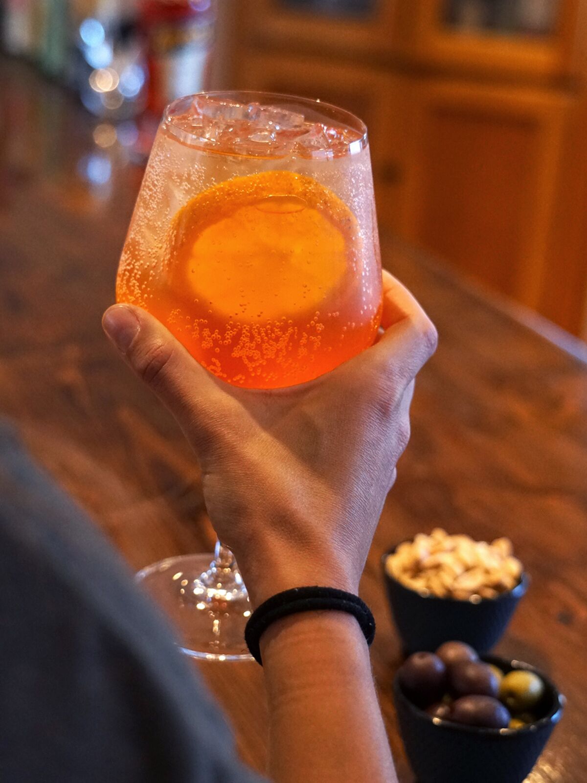 Hand holding an orange drink with ice next to bowls of peanuts and olives