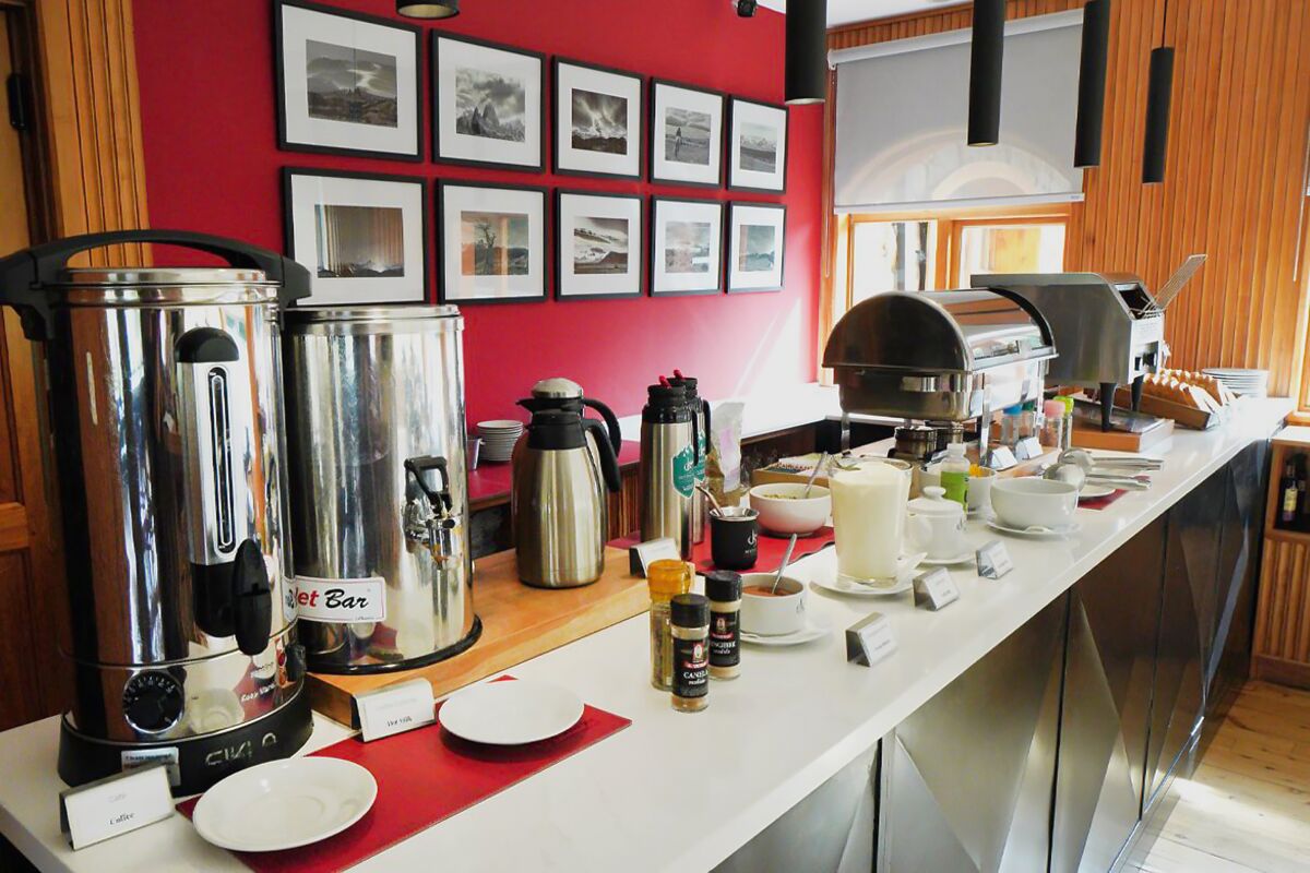 Breakfast counter with hot water urns, a toaster and framed photos on a red wall