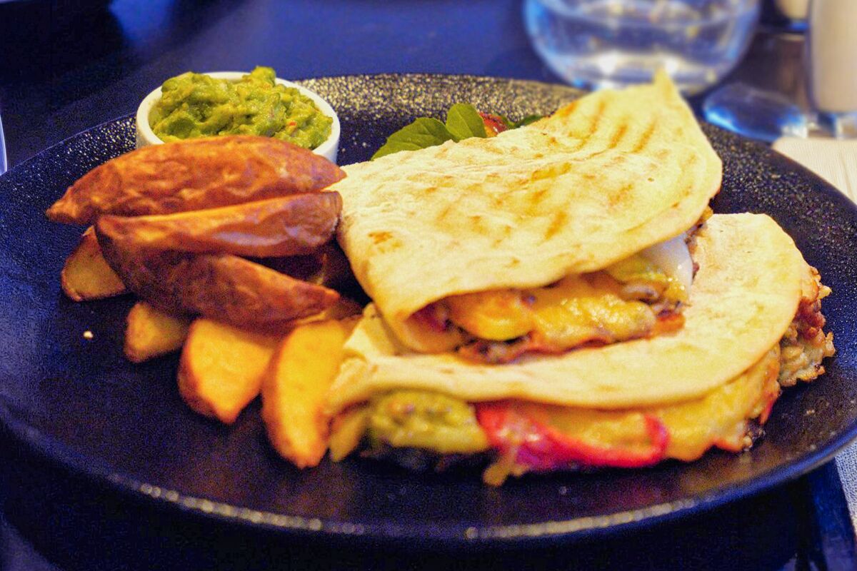 Golden quesadilla with potato wedges and guacamole on a dark plate