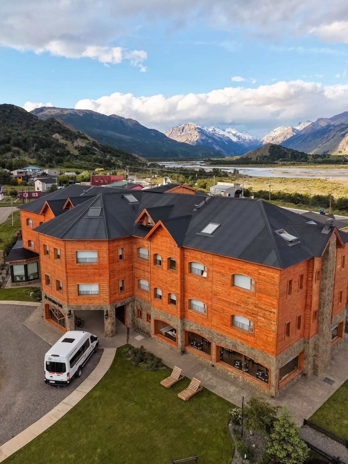 Aerial view of the hotel with the minibus at the entrance and the valley with snowy peaks behind