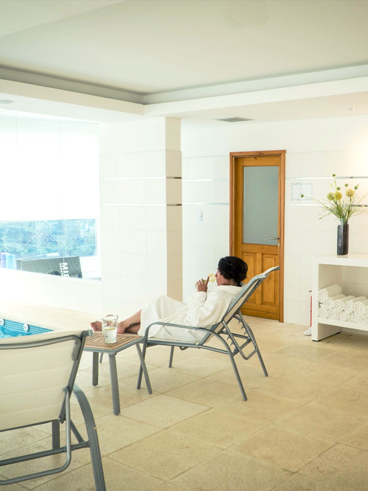 Guest in a bathrobe resting on a lounger next to the indoor pool