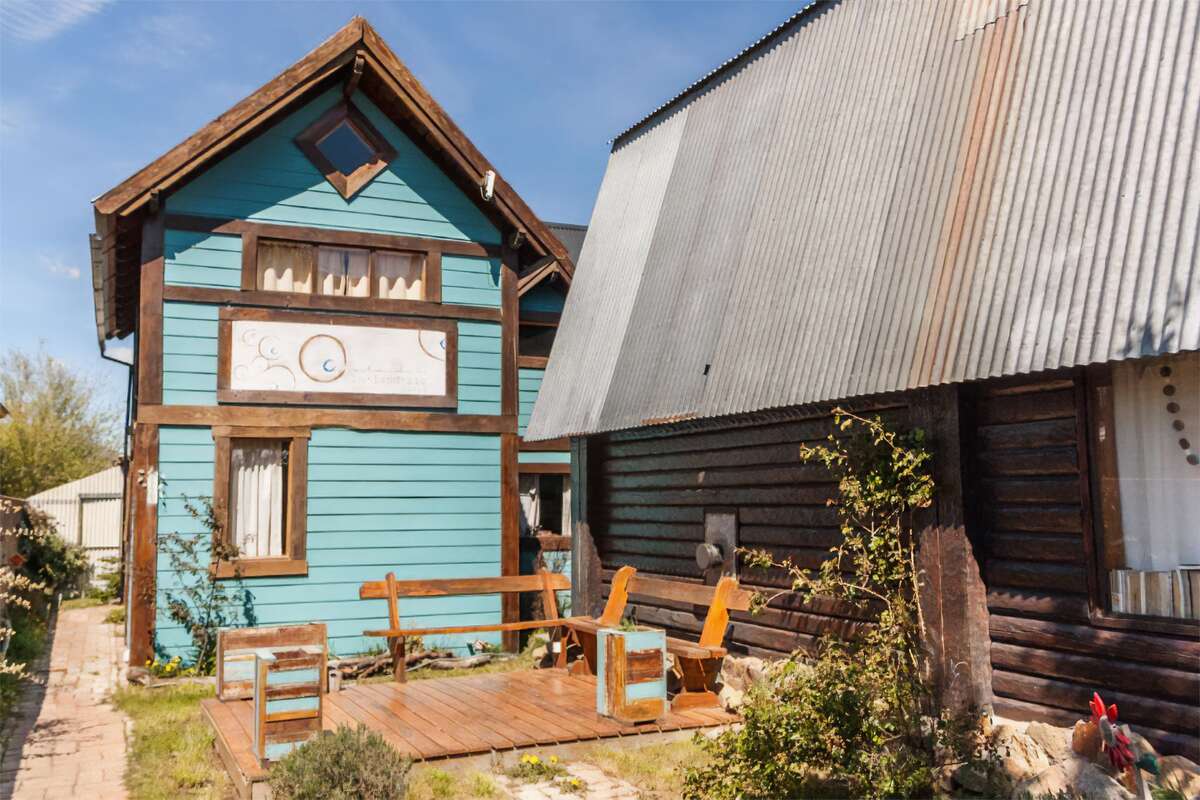 Two-story light-blue wooden cabins with a deck and benches in the garden