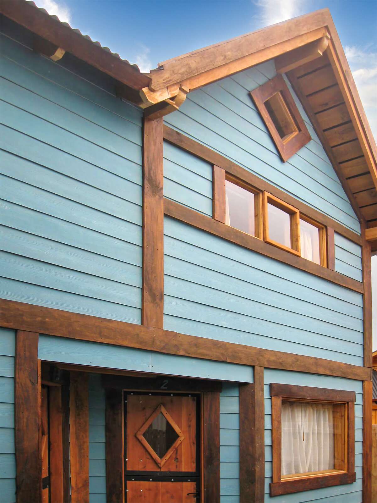Front of a two-story light-blue cabin with a wooden door