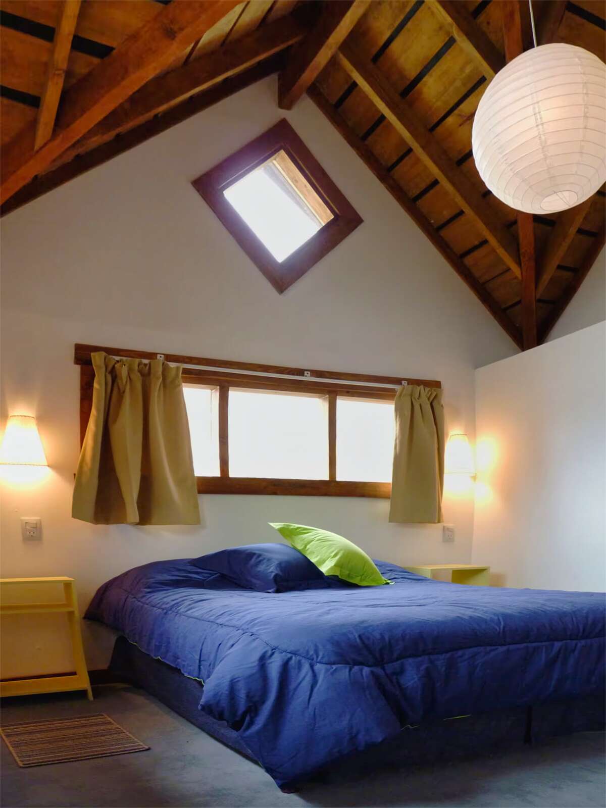 Bedroom under a wooden ceiling with a double bed and a roof window