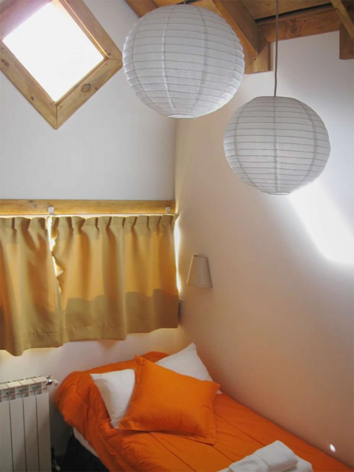 Single bed under a roof window with paper lamps