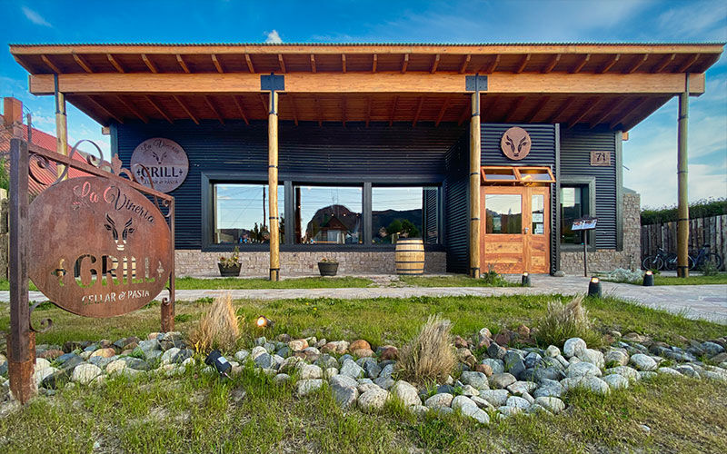 Frente de madera del restaurante con el cartel de La Vinería Grill y un jardín de piedras