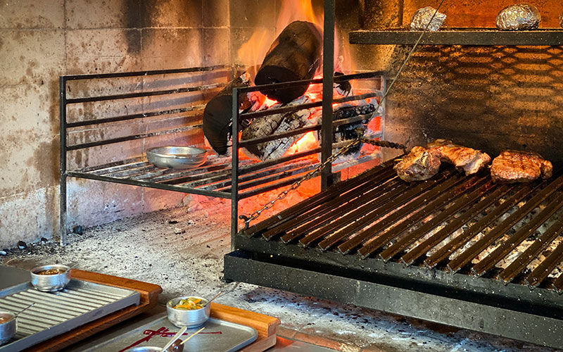 Parrilla a leña con brasas encendidas y cortes de carne asándose