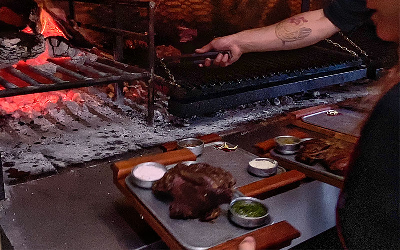 Parrillero sirviendo un corte de carne en una tabla con salsas