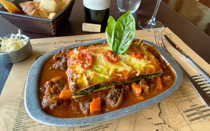 Lasagna de verduras con ragú servida en fuente con vino tinto