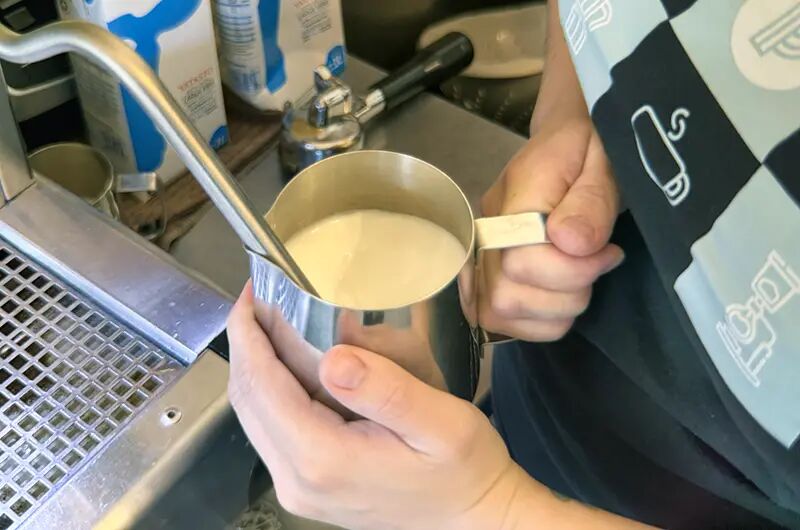 Barista calentando leche en una jarra de acero