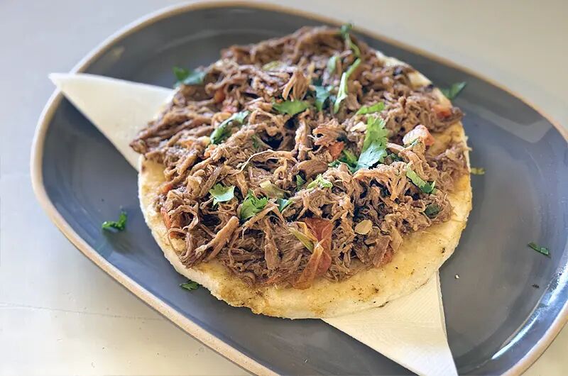 Arepa cubierta de carne desmechada en un plato gris
