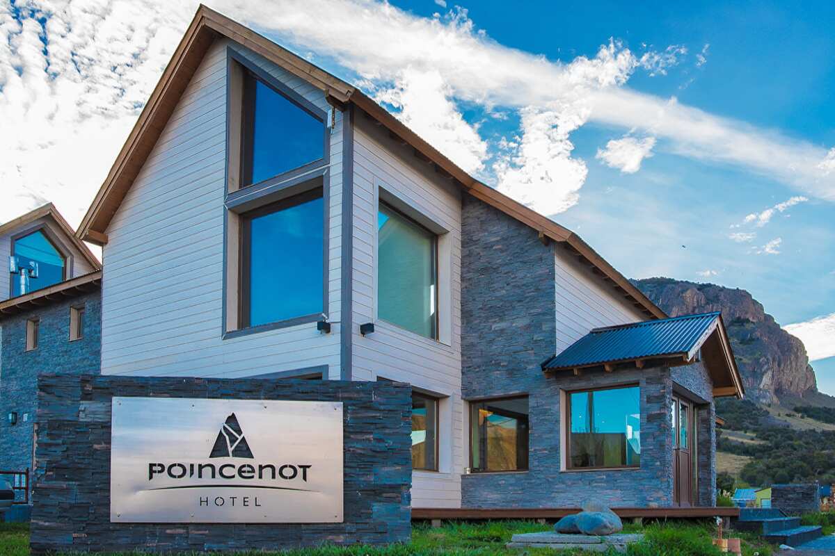 Hotel Poincenot façade with its sign on a stone wall, light siding and a mountain behind