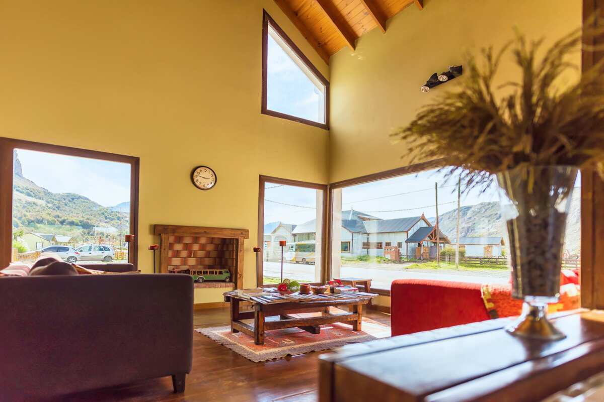 Lounge with sofas, a wooden table, a fireplace and large windows facing the village and the mountains