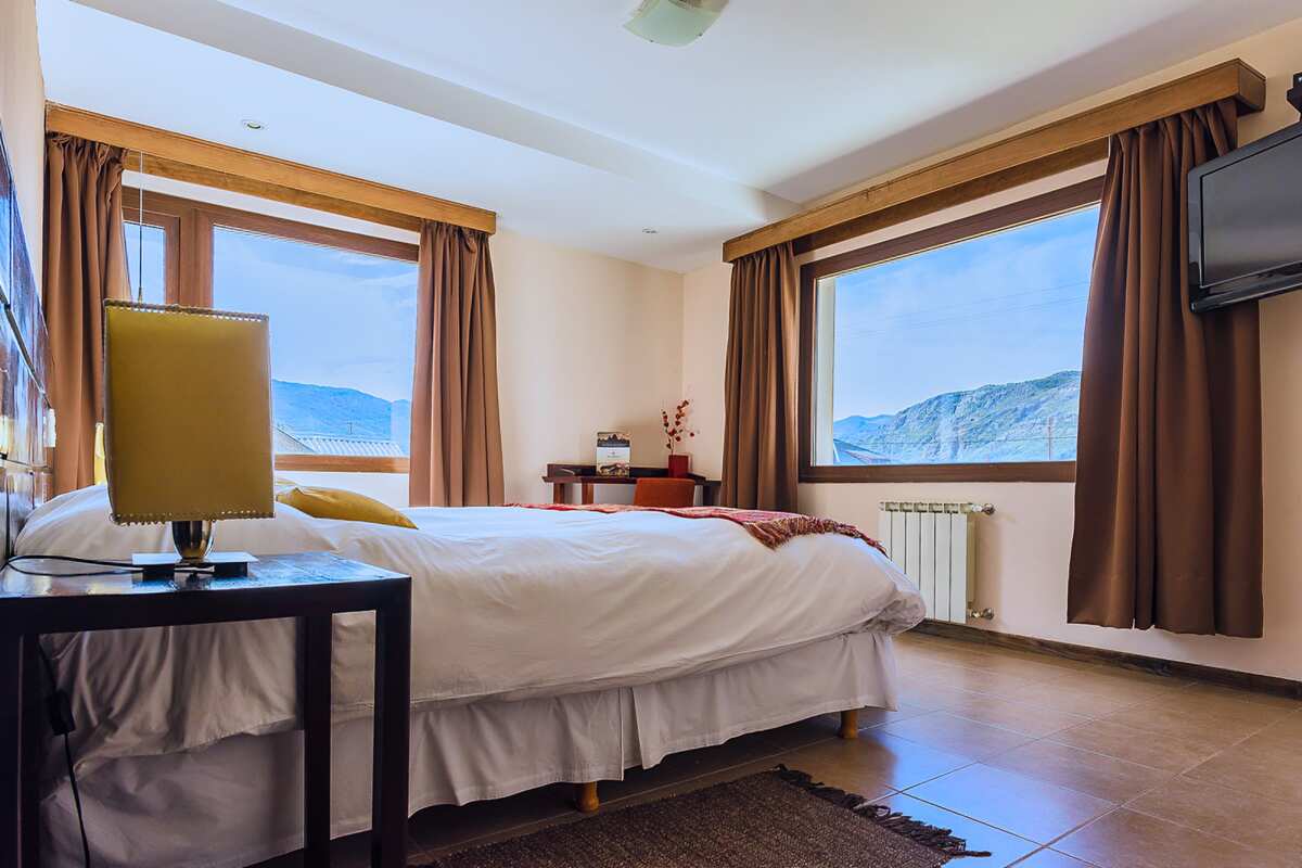 Spacious room with a double bed, TV, radiator and two large windows with mountain views
