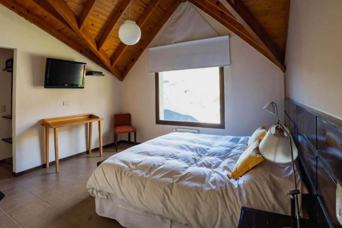 Upper-floor room with a pitched wooden ceiling, double bed, console table and TV