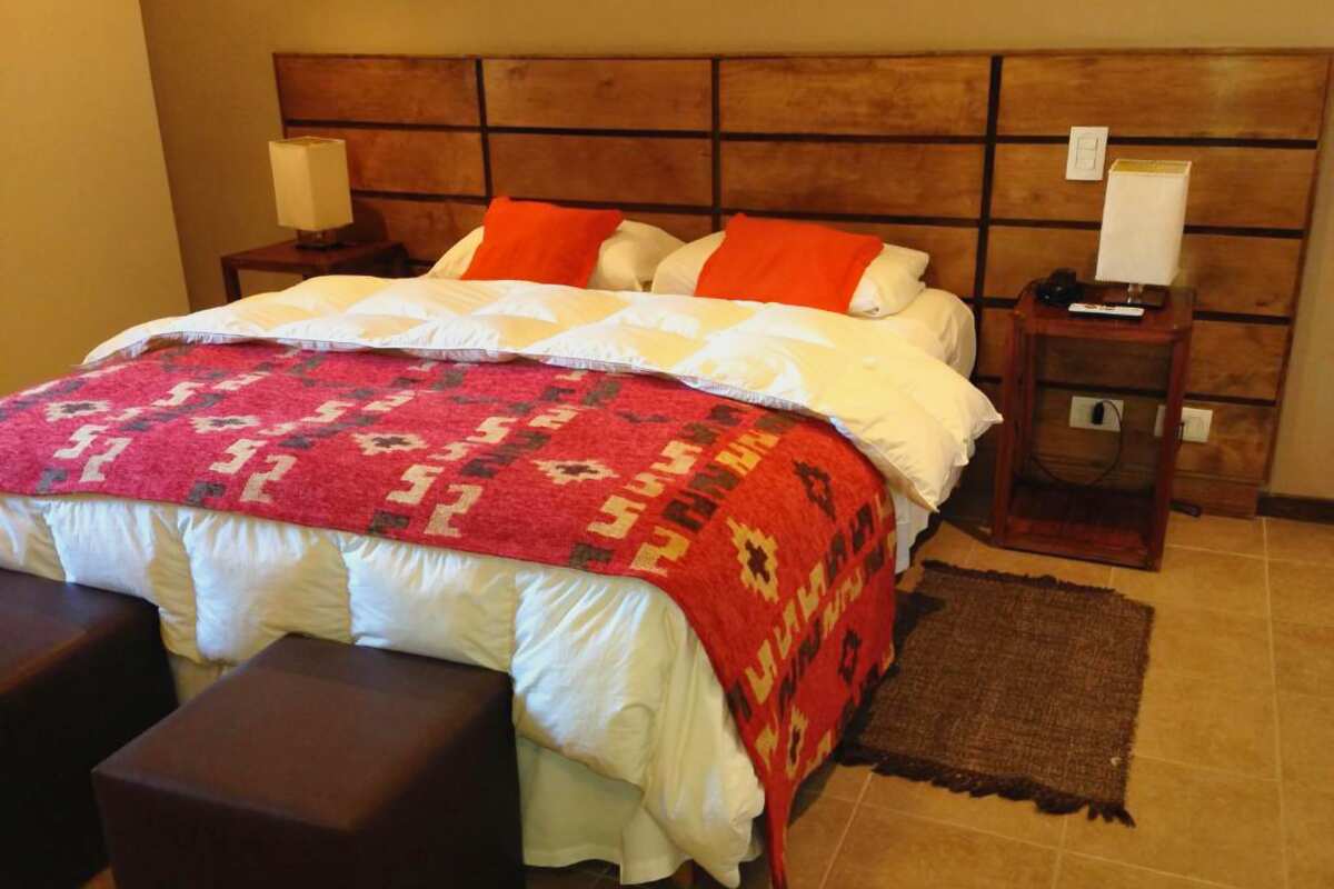 Double bed with a Patagonian-pattern blanket, red cushions and a wooden headboard