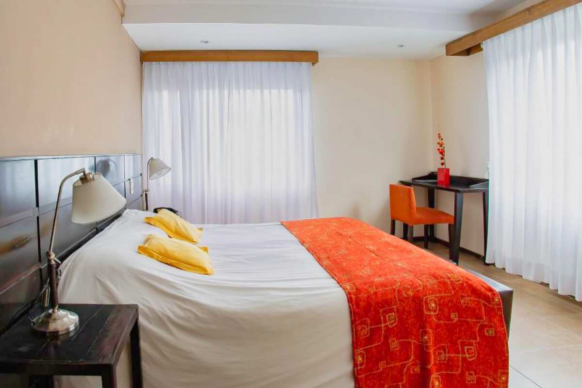Double bed with an orange bed runner, reading lamp and a desk by the window