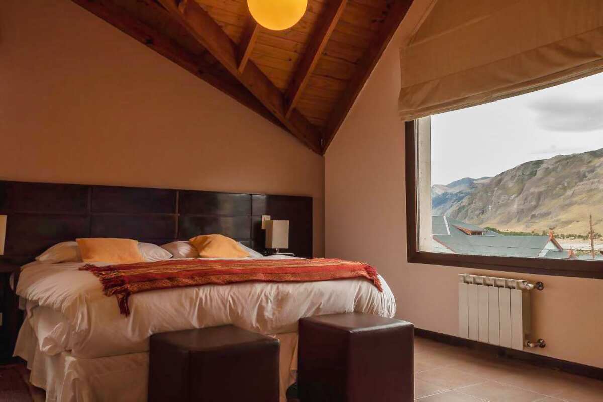 Room under a wooden ceiling with a double bed, a radiator and a window facing the mountains