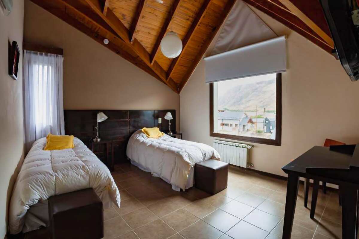 Room with two single beds under a wooden ceiling and a window facing the village