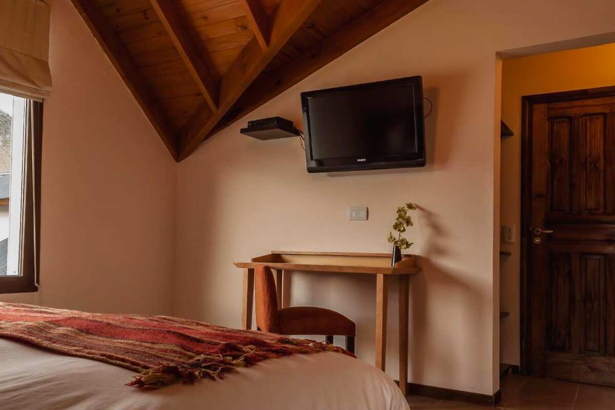 Corner of a room with a wooden desk, TV and pitched ceiling