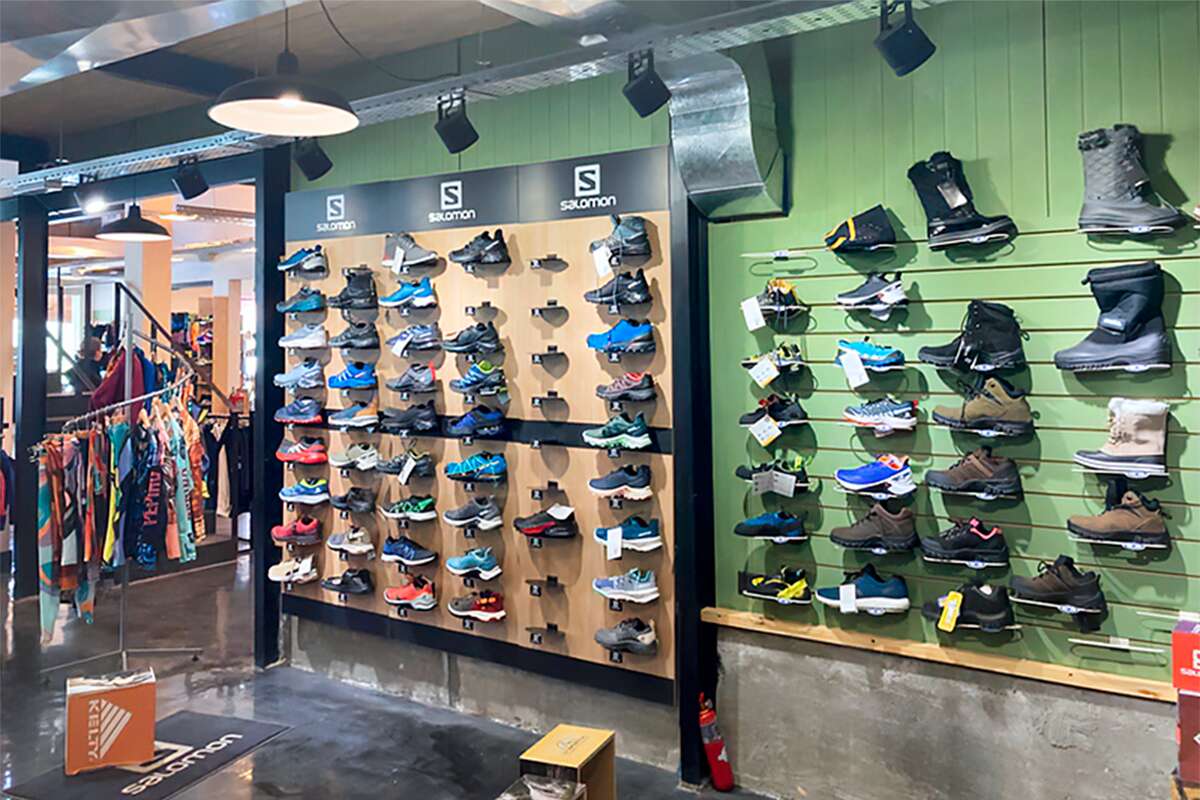 Pared de zapatillas de trekking Salomon y botas de invierno exhibidas en paneles