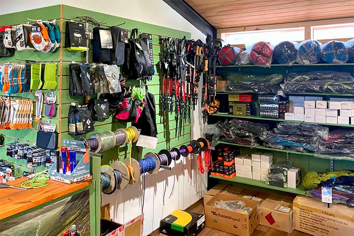 Planta alta: pared de equipo de escalada con cuerdas en carretes, piquetas, guantes Black Diamond y estantes con bolsas de dormir