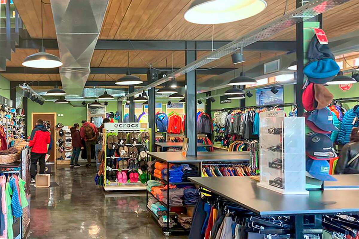 Salón de ventas con camperas colgadas, exhibidor de calzado Crocs y gorros