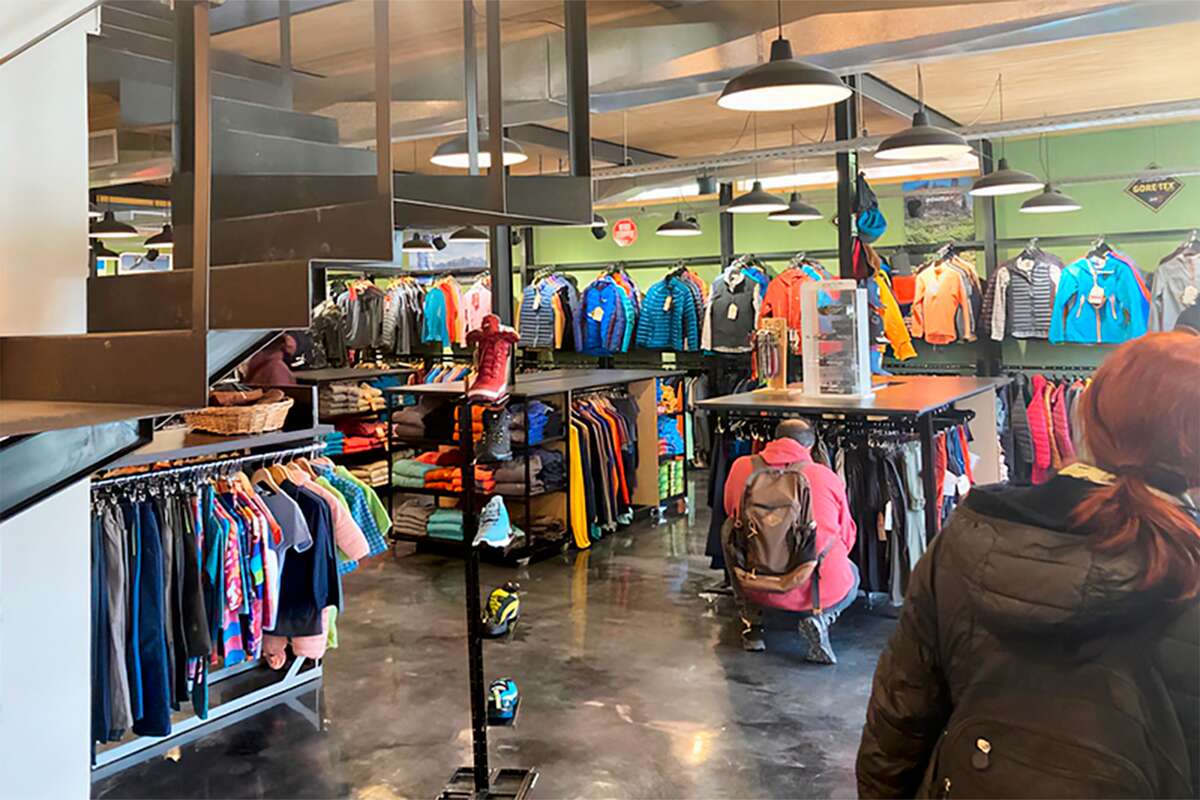 Clientes recorriendo percheros de camperas y mesas con ropa doblada