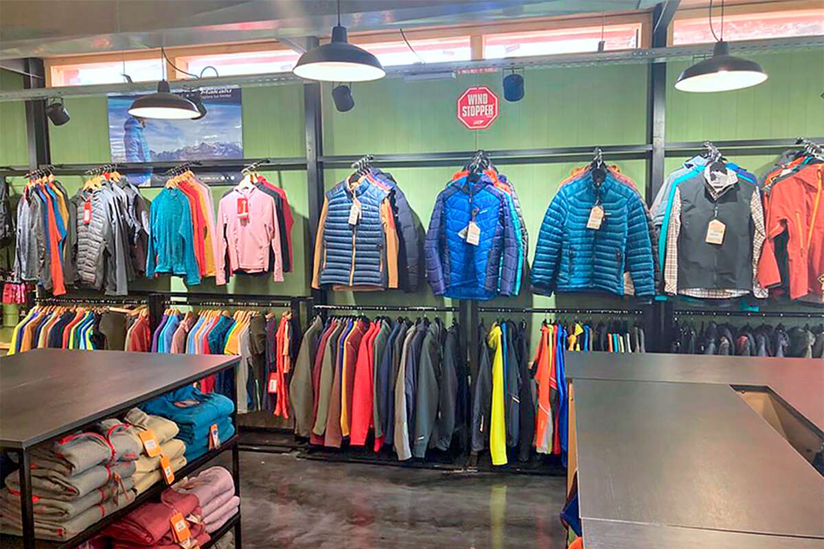 Camperas de pluma y chalecos colgados sobre una pared verde, con cartel de Windstopper